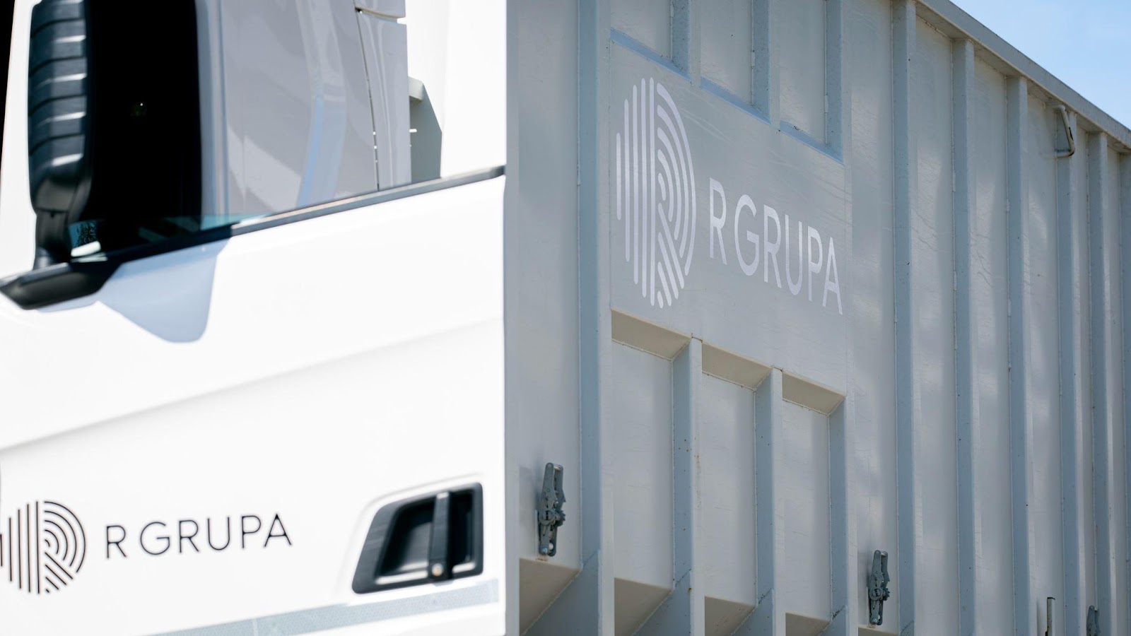 Baltas kravas automašīnas virsbūve ar vairākiem uzņēmuma R GRUPA logotipiem.