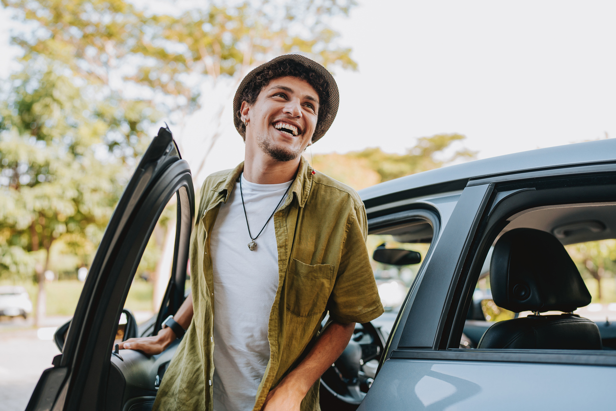 A young driver standing next to a car and smiling. Young renter fee explained in the following paragraph.